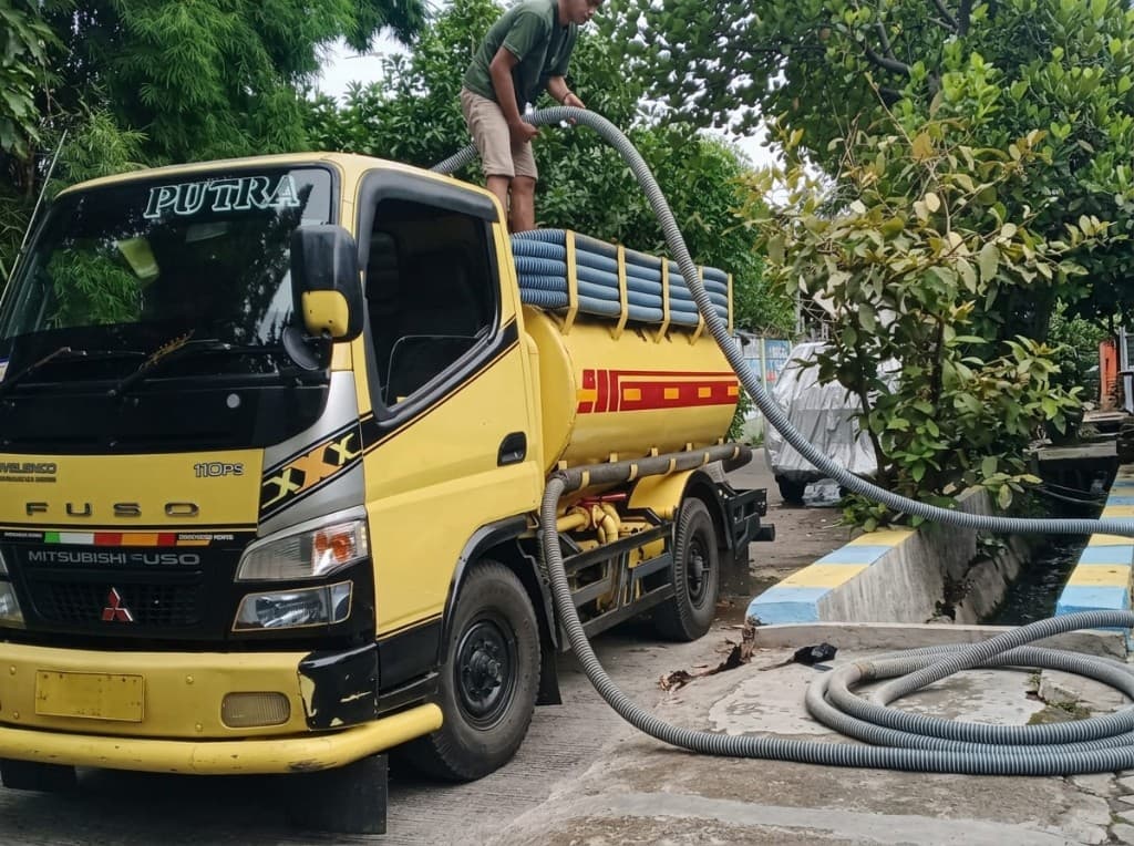 Teknisi di atas tangki menarik selang panjang di lokasi kerja.