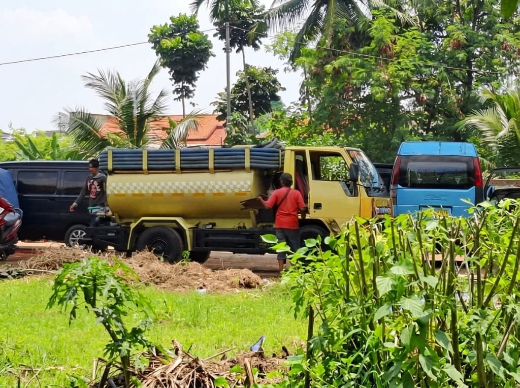 Truk tangki di lahan terbuka dengan selang tergulung di atas tangki.