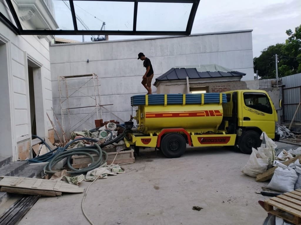 Truk sedot di proyek pembangunan, selang terpasang di halaman.