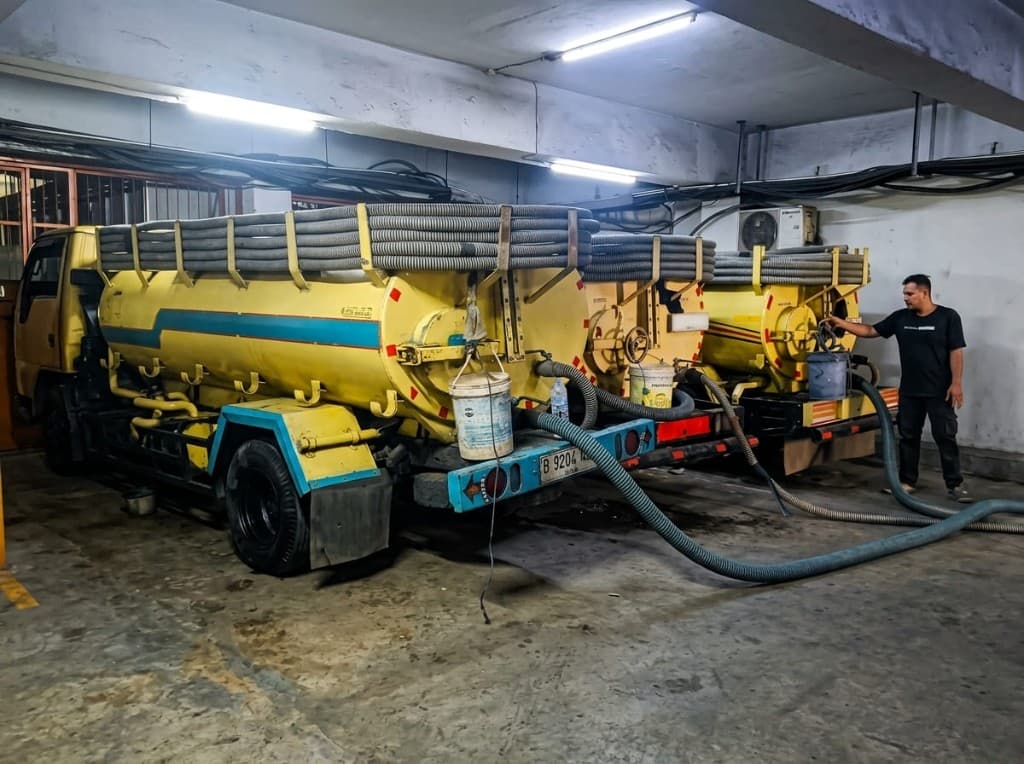 Dua truk tangki di basement dengan selang terpasang ke saluran.
